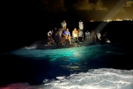 Survivors of a migrant boat that capsized perch on the overturned vessel off the coast of New Providence island, Bahamas