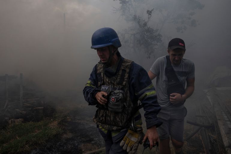 A firefighter walks with of a resident through smoke coming from a house on fire, after cluster rockets hit a residential area, in Konstantinovka, eastern Ukraine on Saturday, July 9, 2022 [Nariman El-Mofty/AP]