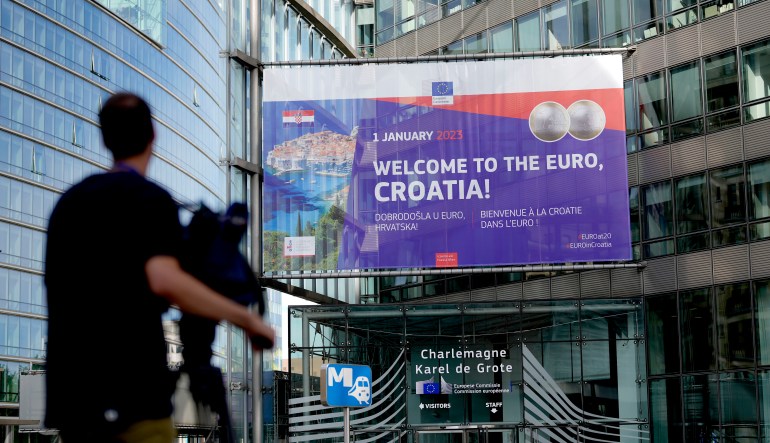 A video journalist films a banner welcoming Croatia to the euro in front of EU headquarters in Brussels