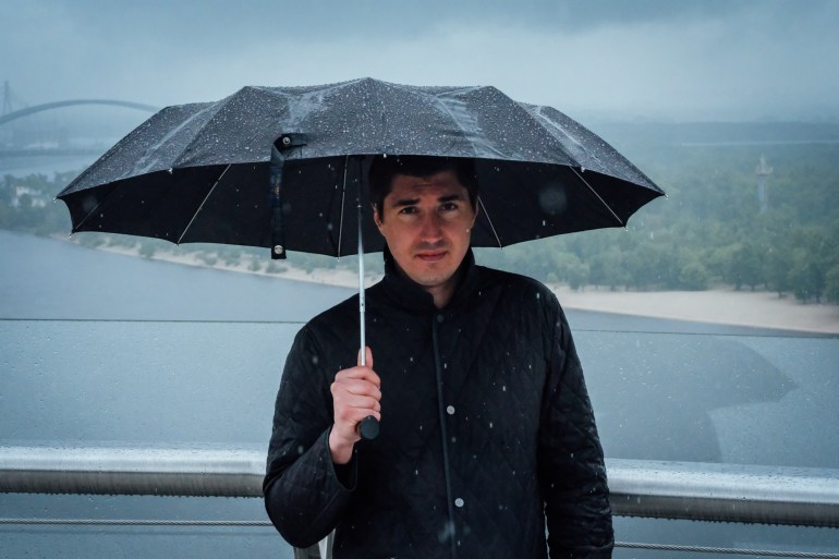 A photo of Oleksandr Nikoriak holding an umbrella over his head in the rain.