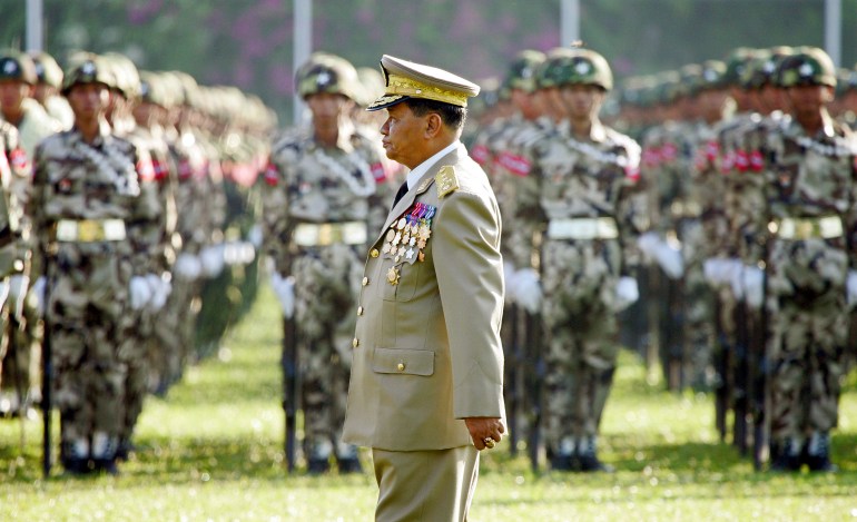 Than Shwe in military dress walks in front of troops standing to attention