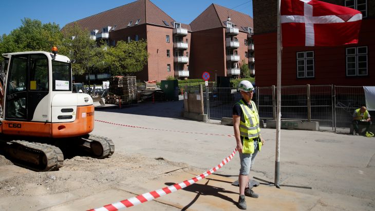 A worker stands beside a Danish flag on a construction site of new housing being built next to Mjolnerparken, a housing estate that features on the Danish government's "Ghetto List", in Copenhagen, Denmark