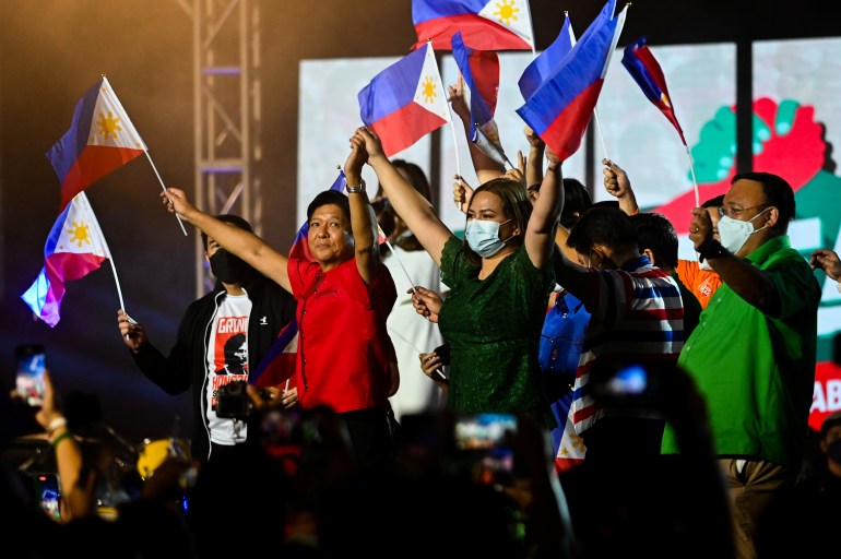 Philippine presidential candidate Ferdinand Marcos Jr., son of late dictator Ferdinand Marcos, and vice-presidential candidate Sara Duterte-Carpio, daughter of Philippine President Rodrigo Duterte, raise their hands as they hold flags, during the first day of campaign period for the 2022 presidential election