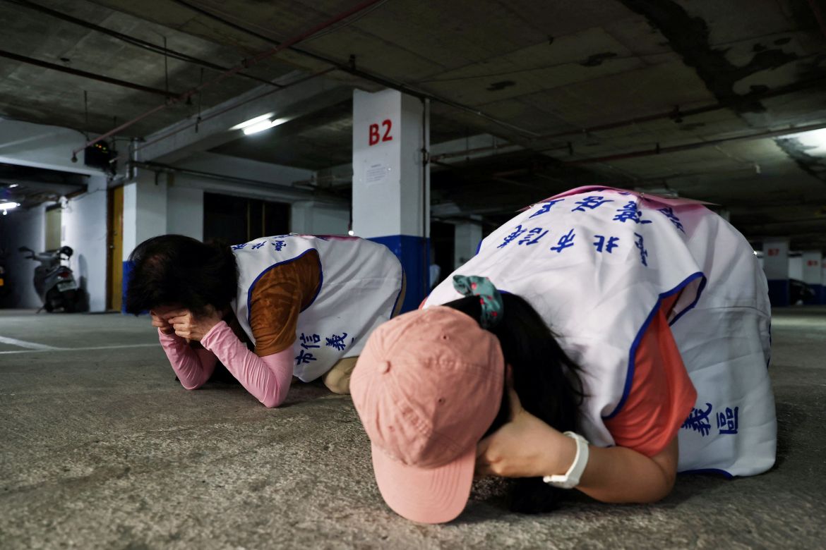 People demonstrate taking shelter with their hands covering their eyes and ears while keeping their mouth open, during a drill at a basement parking lot that will be used as an air-raid shelter