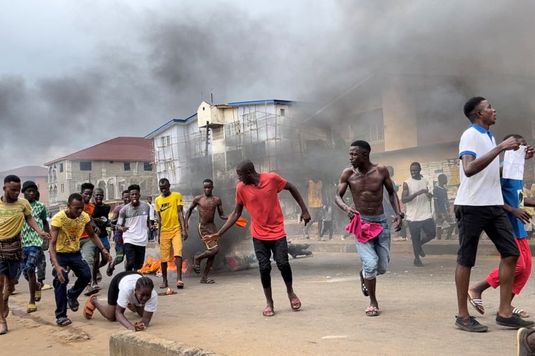 Sierra Leone protesters run among billowing smoke.