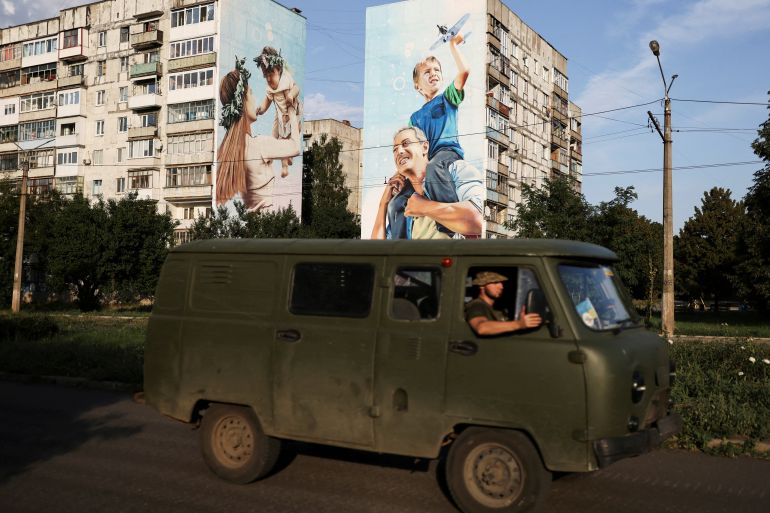Ukraine servicemen drive past a mural of a family on damaged buildings in Bakhmut