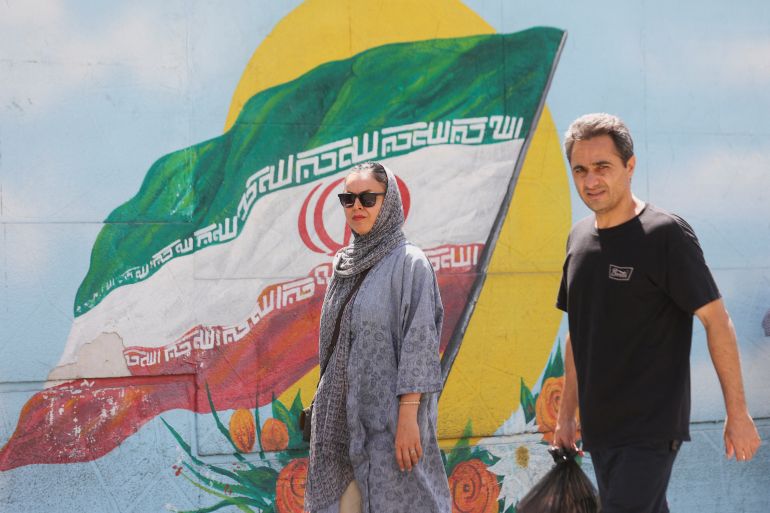 Two Iranians walk in front of a mural of the Iranian flag on a wall