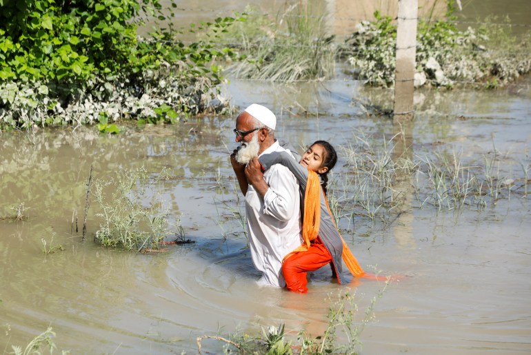 A man wades through flood waters carrying his grand daughter in Charsadda.