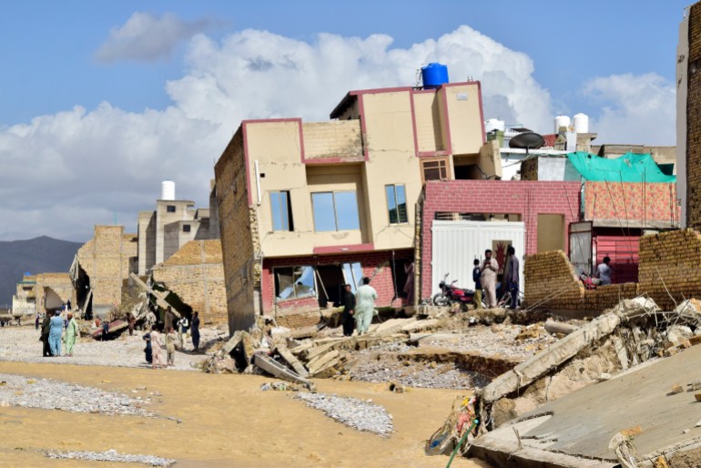 People stand in their partially damage homes caused by flooding after heavy rains in Quetta.