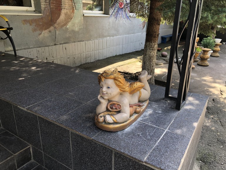 A photo of a figurine of an angel on it's stomach outside a building.