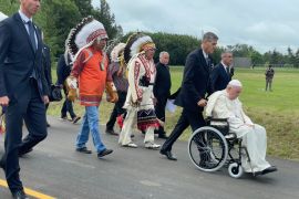 A photo of someone pushing the pope in a wheelchair with people all around.