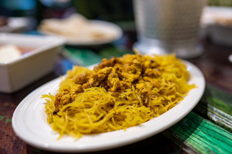 A closeup of a plate of vermicelli cooked to a yellowish tinge, topped with spiced scrambled eggs cooked all the way through