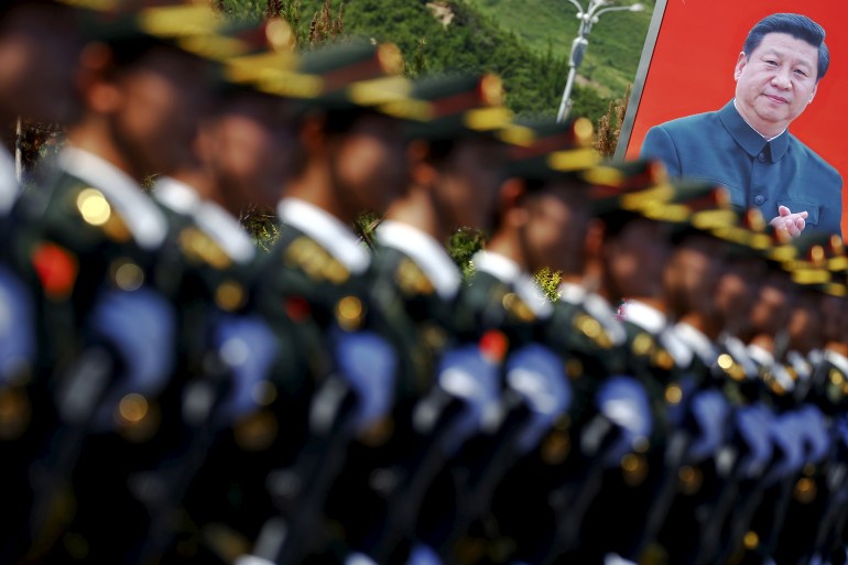 China military formation out of focus in the foreground with a large banner featuring a photo of Xi Jinping in the background.