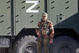 A service member of pro-Russian troops stands next to a military vehicle with the letter "Z".