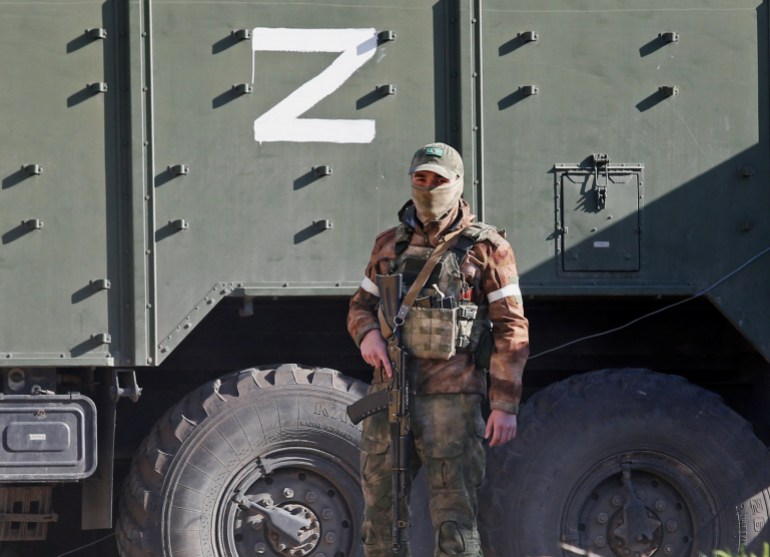 A service member of pro-Russian troops stands next to a military vehicle with the letter "Z".