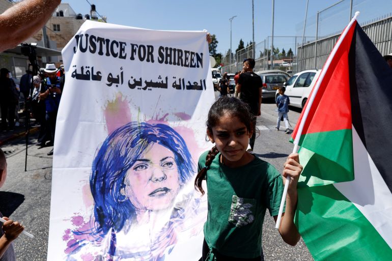 A Palestinian girl holds a Palestinian flag and a banner that reads Justice for Shireen along with the slain journalist's photo.