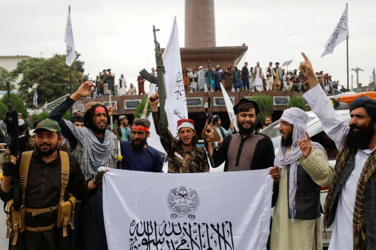 Taliban fighters hold Islamic Emirate of Afghanistan flags on the first anniversary of the fall of Kabul.