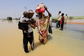People cross the water during a flood in Al-Managil locality, Sudan