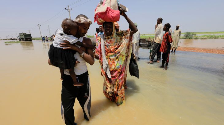 People cross the water during a flood in Al-Managil locality, Sudan