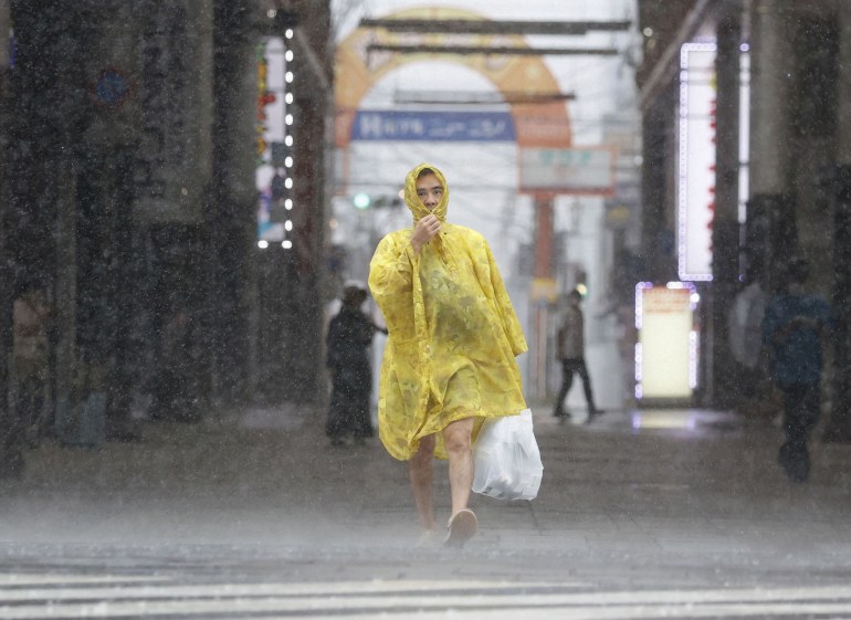 A man in a yellow disposable rain coat is lashed by rain as he carried shopping in a street in Kagoshima