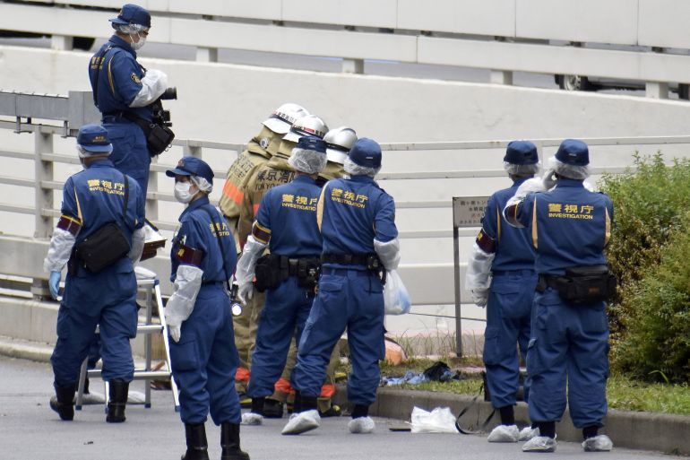 Police officers in blue overalls with 'investigator' written on the back work at the site where a man set himself on fire near the prime minister's office in Tokyo, Japan.
