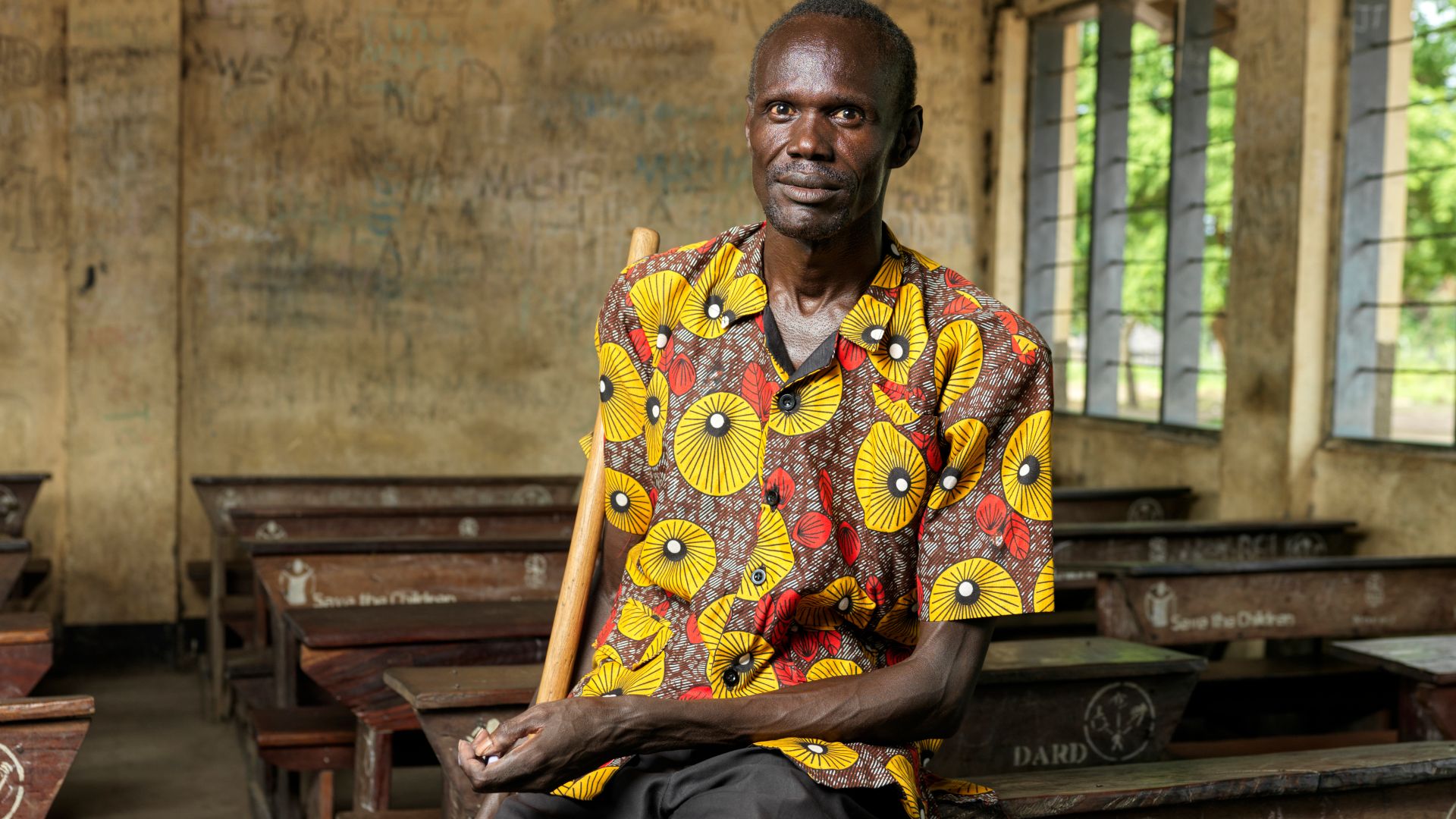 A photo of Clement Makuak sitting on a desk in an empty classroom.