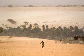 A young girl carries an empty container as she walks across the sands to fill it from a well in Barrah, a desert village in the Sahel belt of Chad