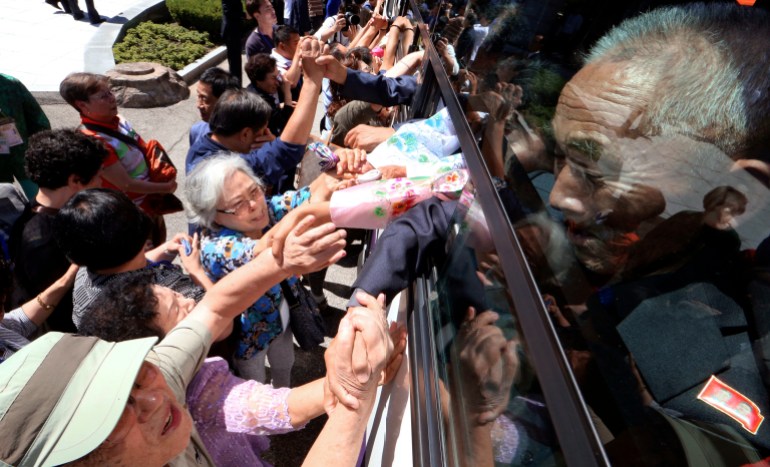 Elderly North Koreans, their faces anguished and some crying, stretch out their hands to grasp those of their relatives in South Korea as they leave on a bus