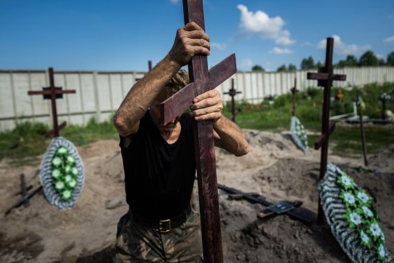 A funeral worker installs a cross with a number plate on the grave of an unidentified civilian killed by Russian troops during the Russian occupation in Bucha near Kyiv, Ukraine, on Wednesday, Aug. 17, 2022. Twenty one unidentified bodies exhumed from a mass grave were buried in Bucha on Wednesday. (AP Photo/Evgeniy Maloletka)