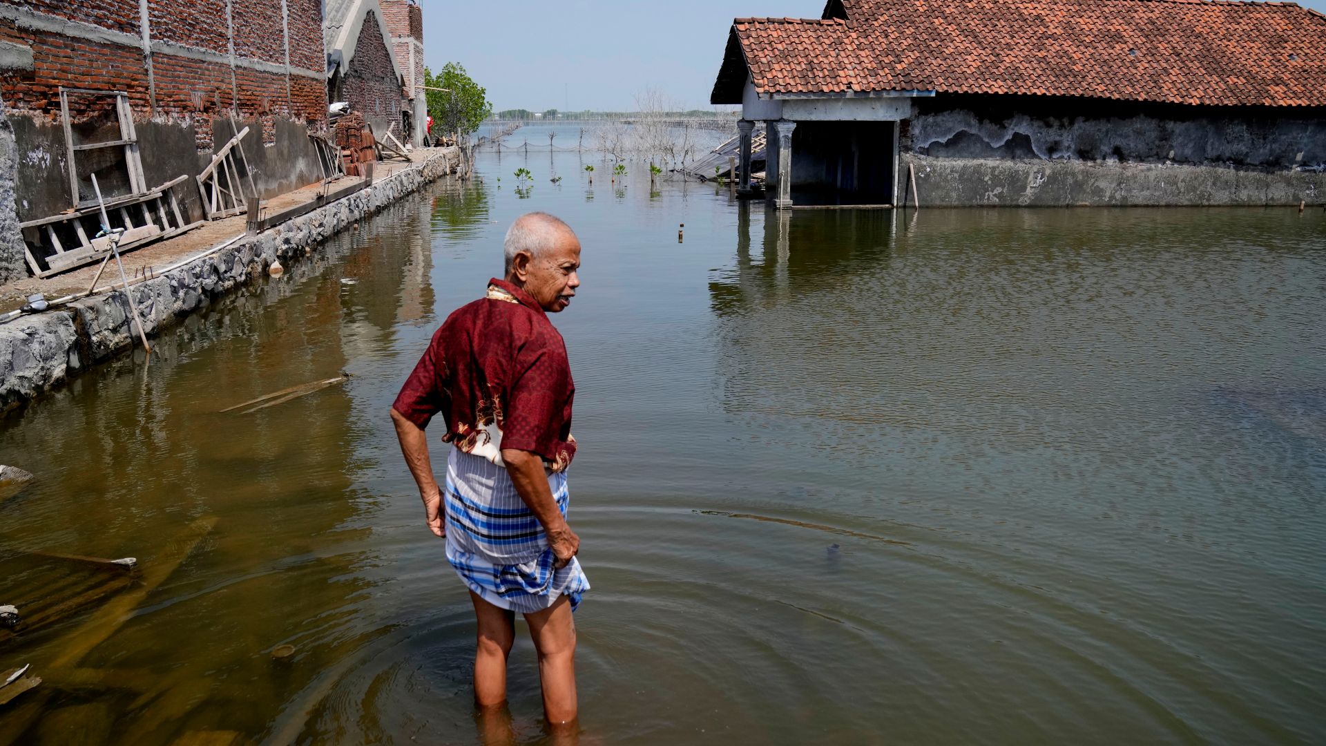 Sukarman walks on a flooded pathway outside his house