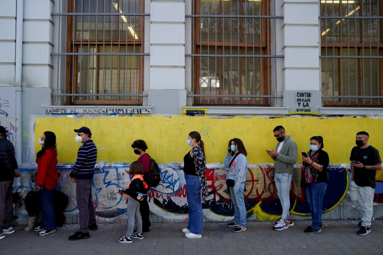 People queue up in front of a yellow wall to vote in the referendum on a new constitution for Chile