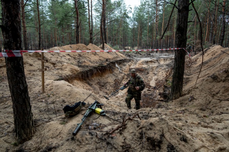 A soldier stands in the mud surrounded by trees where a mass grave was discovered near Izyum, Ukraine.