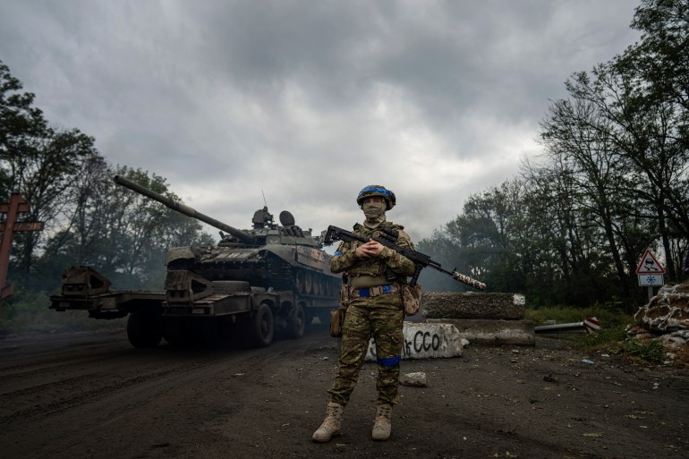 A Ukrainian soldier stands at a checkpoint on a road near Izyum with a tank behind him