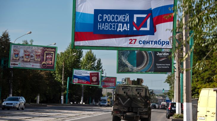 A military vehicle drives along a street with a billboard that reads: "With Russia forever, September 27", ahead of a referendum in Luhansk