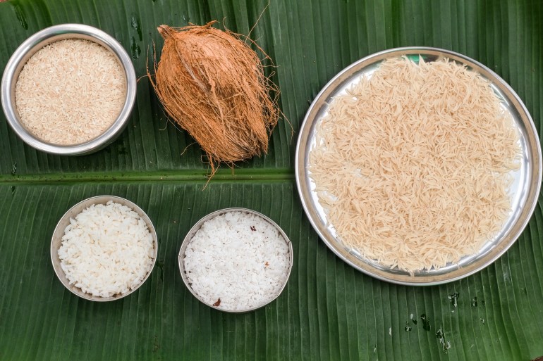 Laid out on a banana leaf are a coconut, a bowl of shredded coconut, two trays of dry rice and a bowl of cooked rice