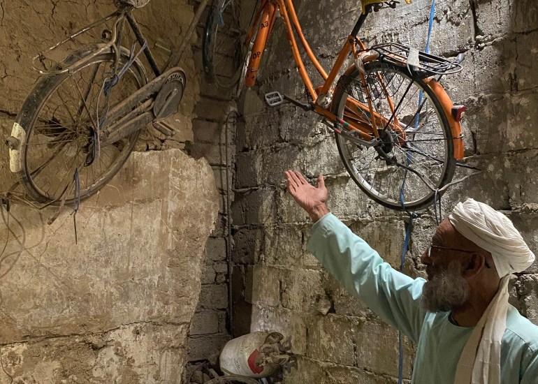 A photo of Haji Nazar Muhammad pointing to a bicycle on the wall with two car tires in the corner.