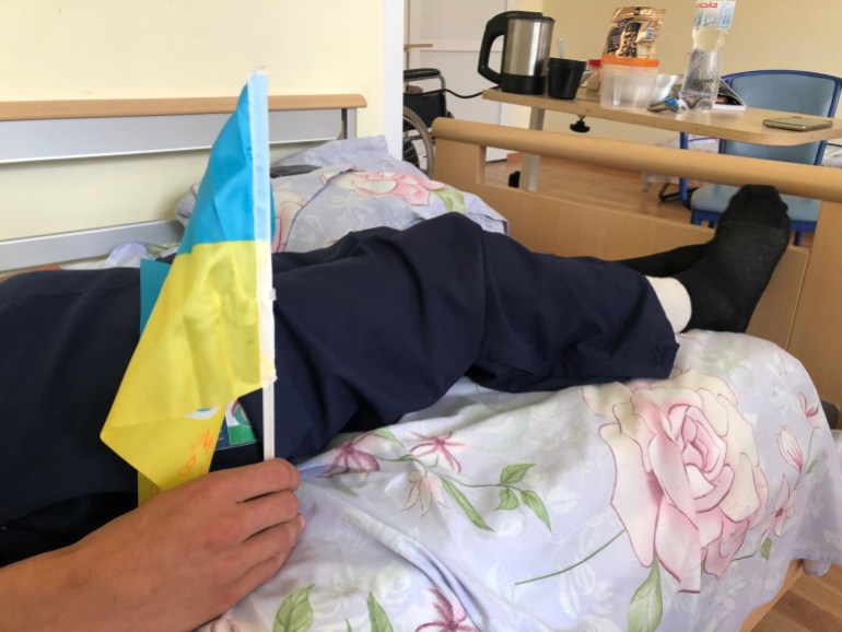 A photo of the lower half of someone lying down with their feet out of the bed whilst holding a Ukrainian flag in one hand,