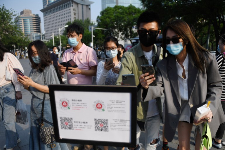 A crowd of people in masks show their phones and green COVID codes to a security guard as they enter a Beijing shopping street