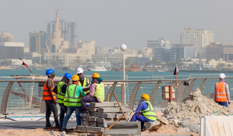 A picture taken on May 21, 2022, shows workers fixing a sidewalk with a backdrop of the Qatari capital Doha, six months ahead of the FIFA World Cup 2022 which the country is hosting. 