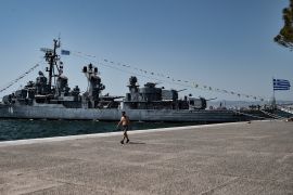 A man walks next to a war ship museum on the waterfront of Thessaloniki