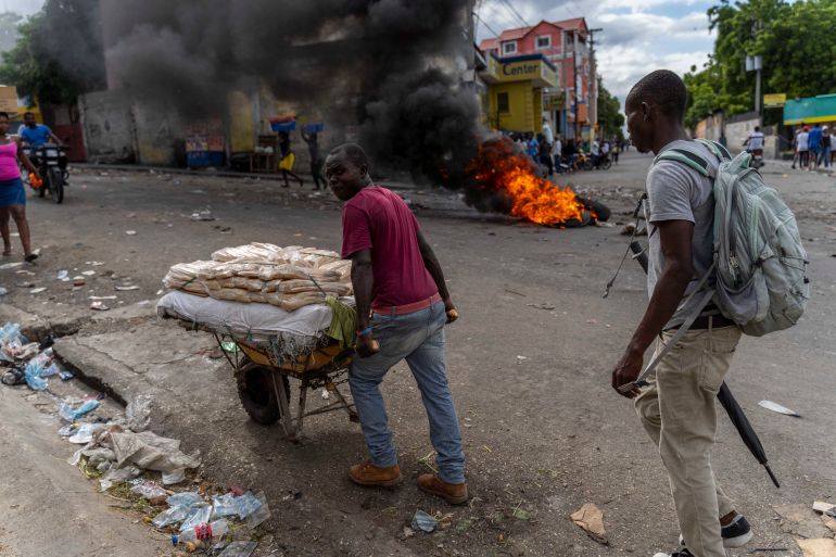A vendor pushes a cart past a burning barricade during a protest in Port-au-Prince, Haiti