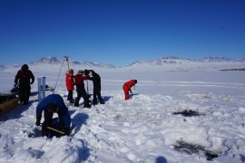 Researchers drilling holes to collect sediment at snow-covered Lake Hazen in Nunavut, Canada.