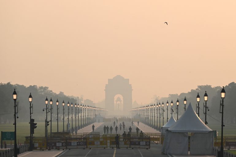 People walk along a road near India Gate amid smoggy conditions in New Delhi on October 25, 2022. - New Delhi woke up to toxic smog on October 25 after Diwali revellers defied a firecracker ban and risked facing jail term to celebrate the annual Hindu festival.