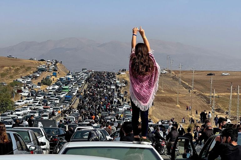 An unveiled woman standing on top of a vehicle as thousands make their way towards Aichi cemetery in Saqez, Mahsa Amini's home