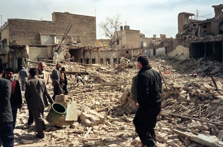 A photo of Iraqi civil defence workers and civilians looking at destroyed houses.
