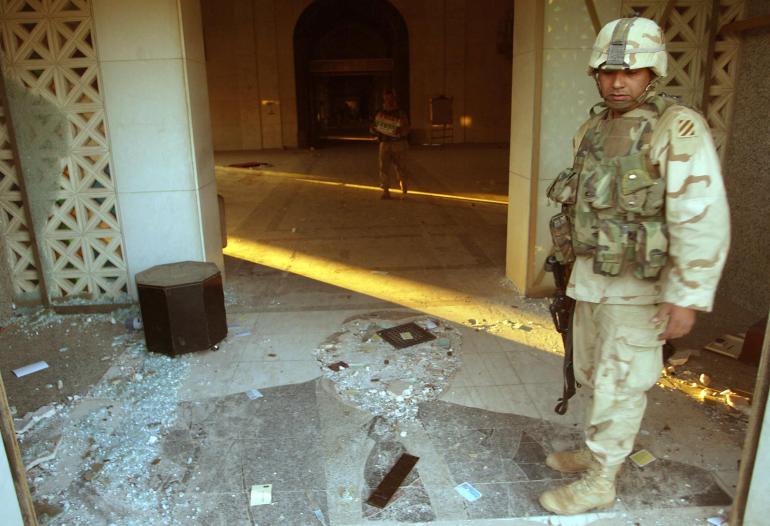 A photo of a US soldier standing near a destroyed mosaic of former US President George Bush.