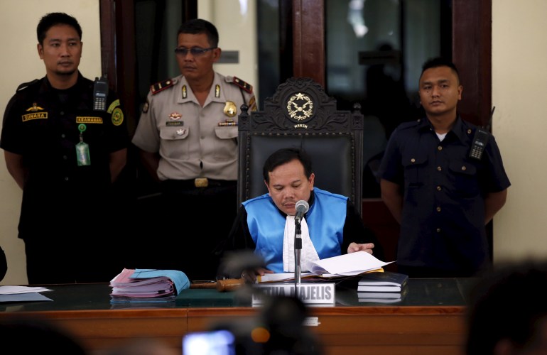 A judge in sky blue robes in an Indonesian court with police standing behind him.