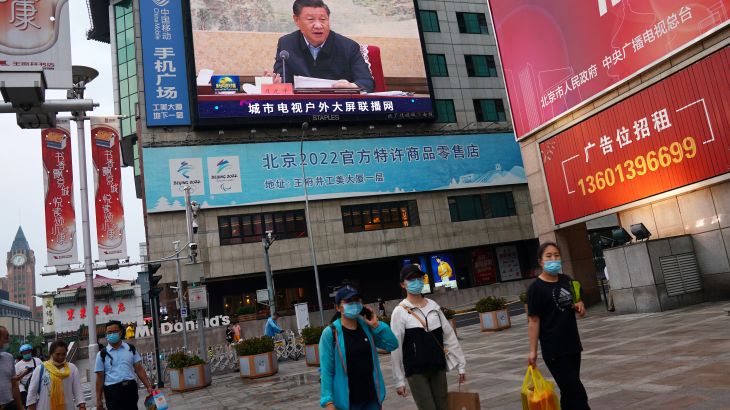 People walk near a screen showing Chinese President Xi Jinping