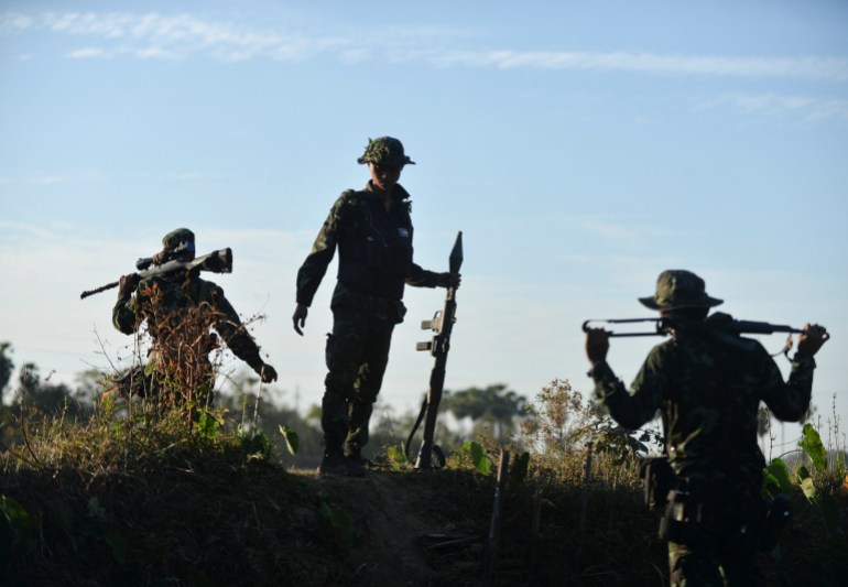 Three soldiers, members of Myanmar's People's Defence Forces, stand with their weapons, silhouetted against the sky.