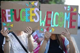Two women hold up signs in bright colours reading 'refugees welcome'